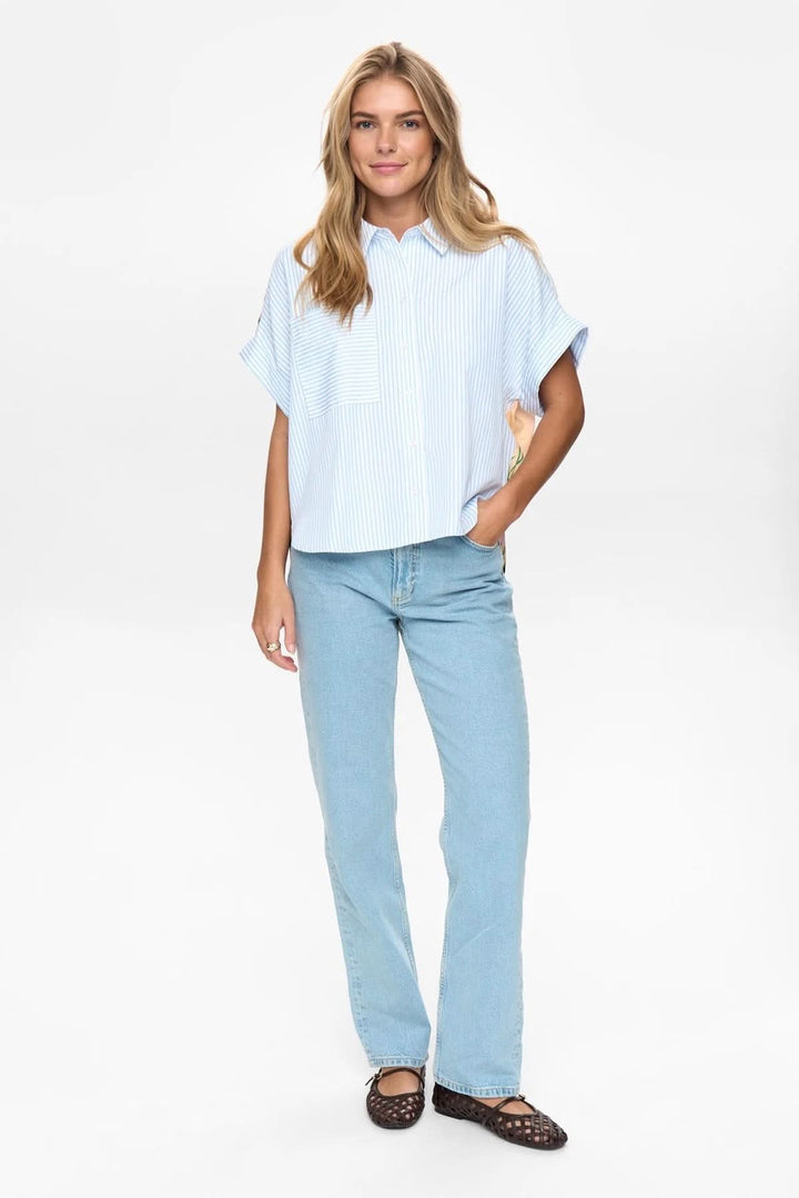 Femme portant une chemise fluide à rayures avec imprimé artistique, manches courtes et col classique, mode décontractée et élégante.