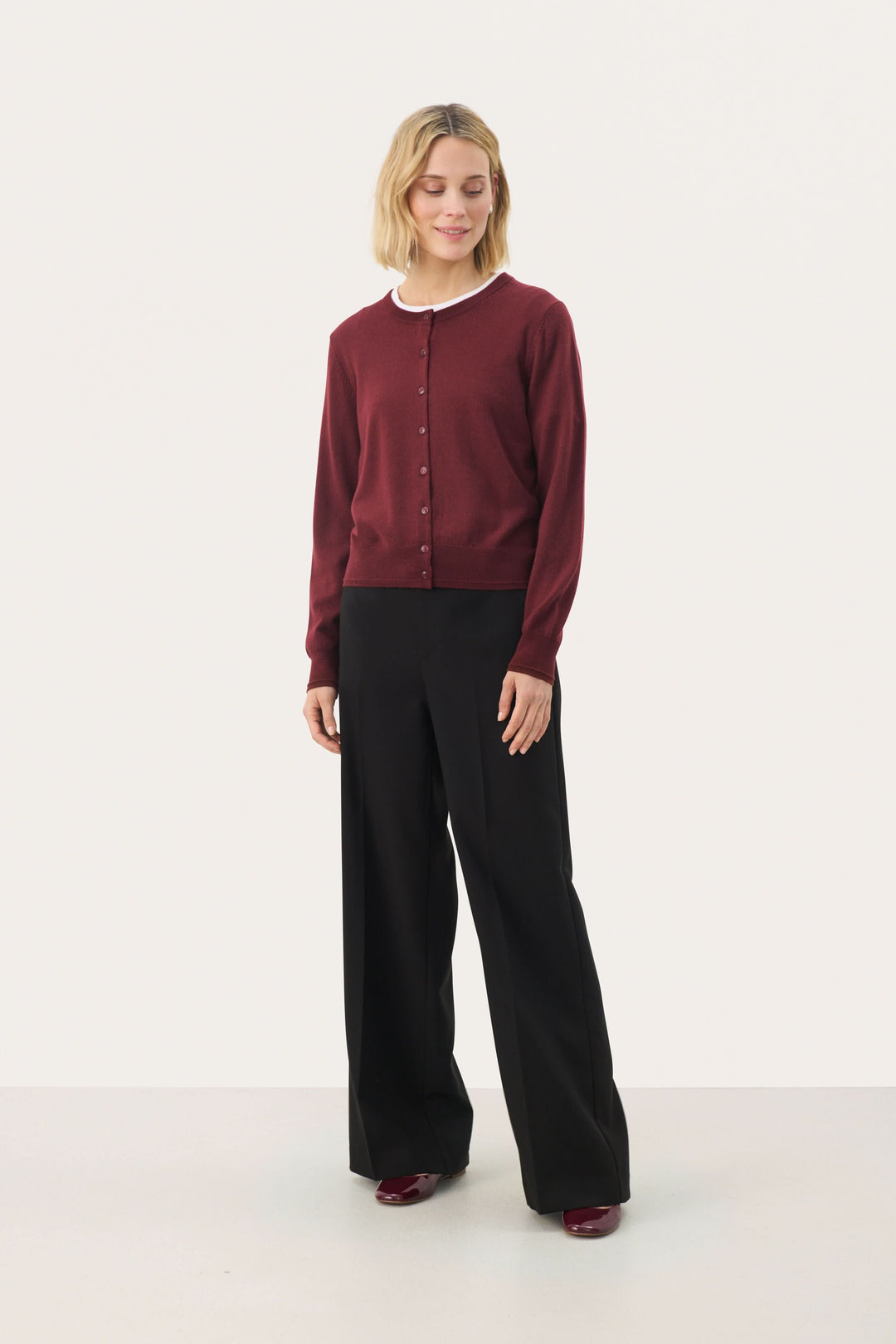 Cardigan Noelani classique à encolure ronde, porté avec un pantalon noir, idéal pour un look de bureau ou décontracté.
