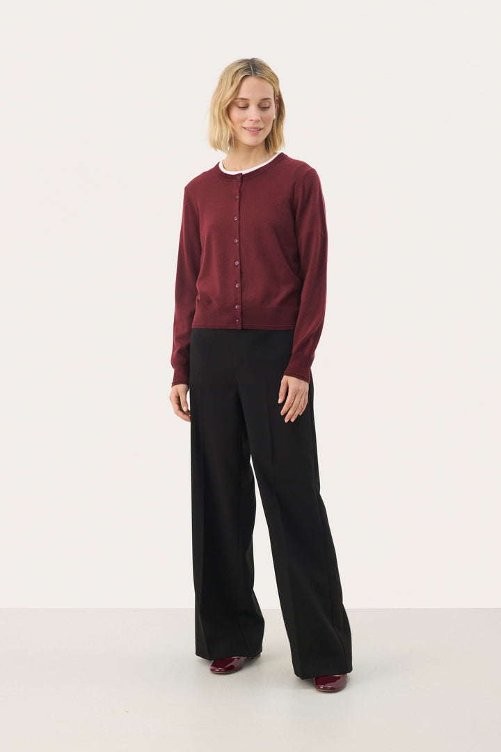 Cardigan Noelani classique à encolure ronde, porté avec un pantalon noir, idéal pour un look de bureau ou décontracté.