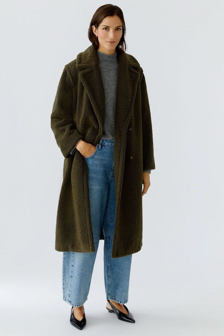 Femme portant un manteau long en tissu bouclette, style moderne et douillet, idéal pour les journées froides avec élégance.