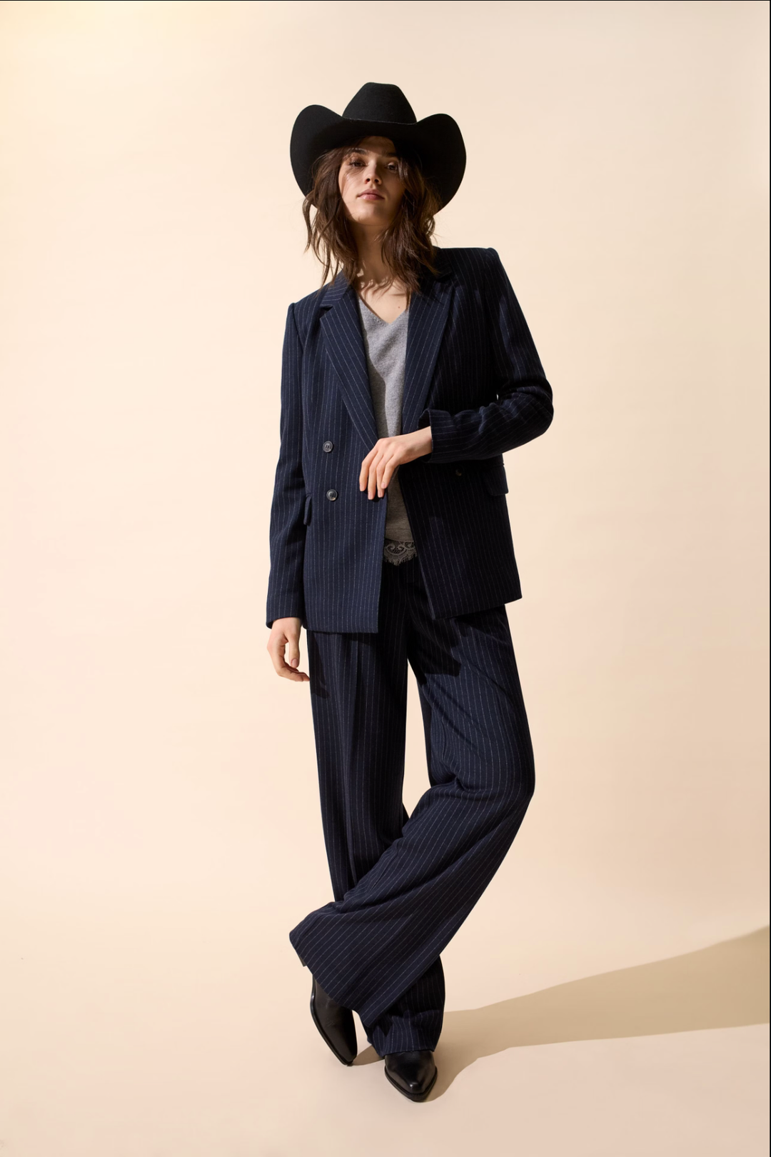 Femme en veston à rayures, pantalon large et chapeau de cowboy, look chic décontracté.