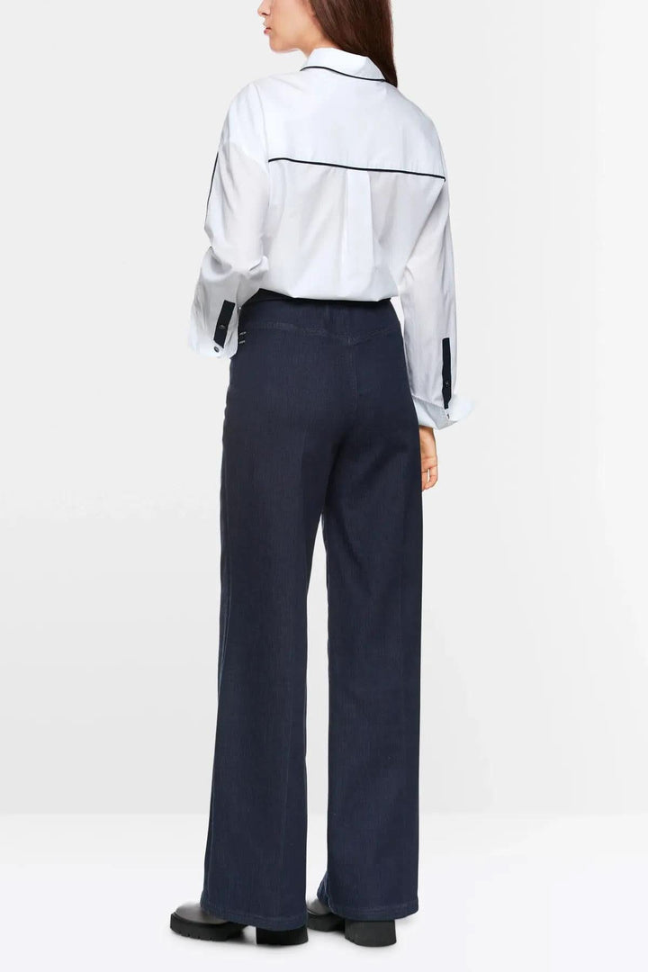 Femme portant un jean évasé WELKOM avec une chemise blanche à l'arrière, style moderne et décontracté.
