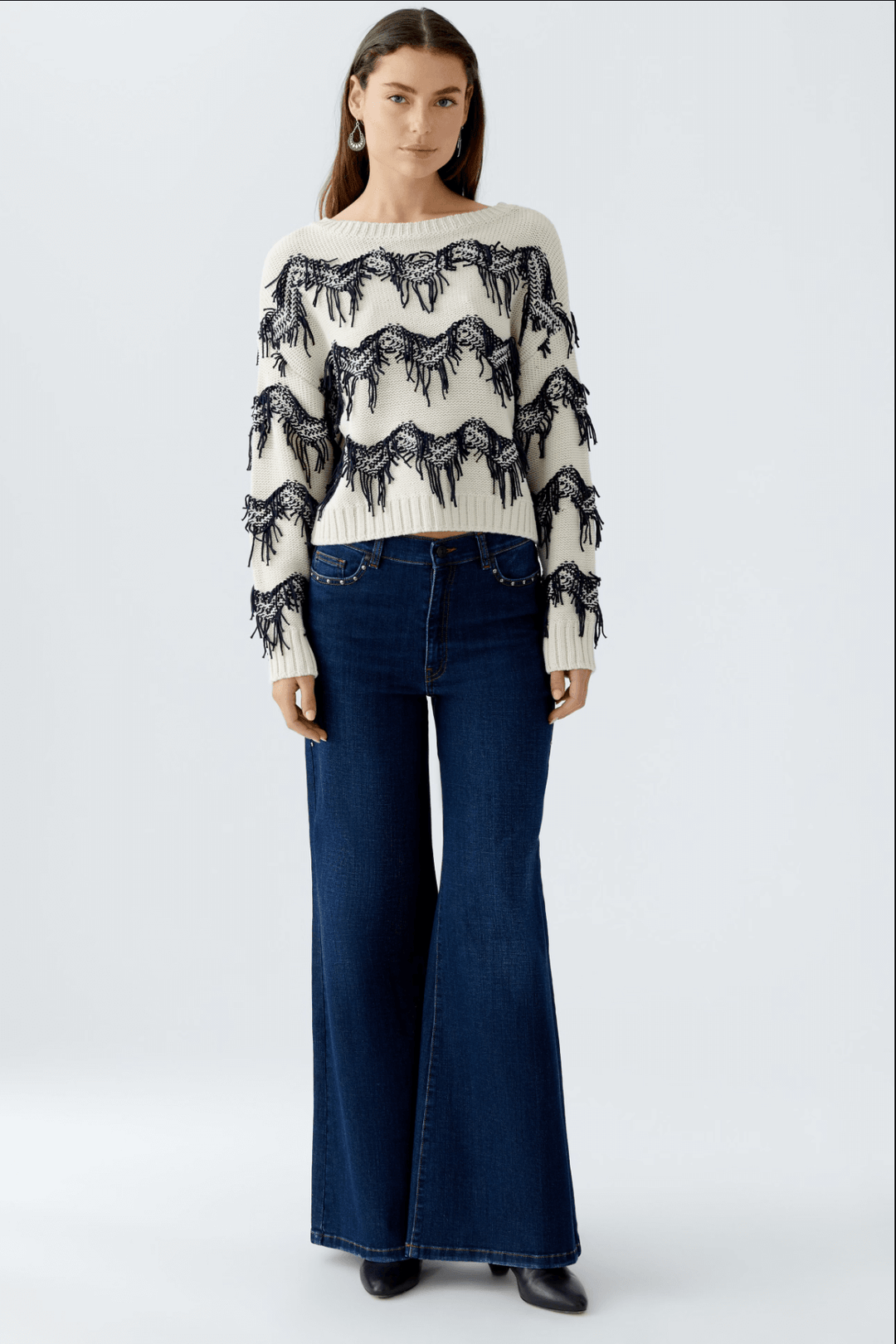 Tricot à motif zigzag avec franges, porté avec un pantalon flare, style moderne et décontracté.