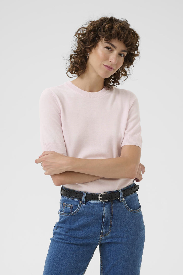 Femme portant un chandail en tricot rose à manches courtes avec jeans bleu, style classique et intemporel.