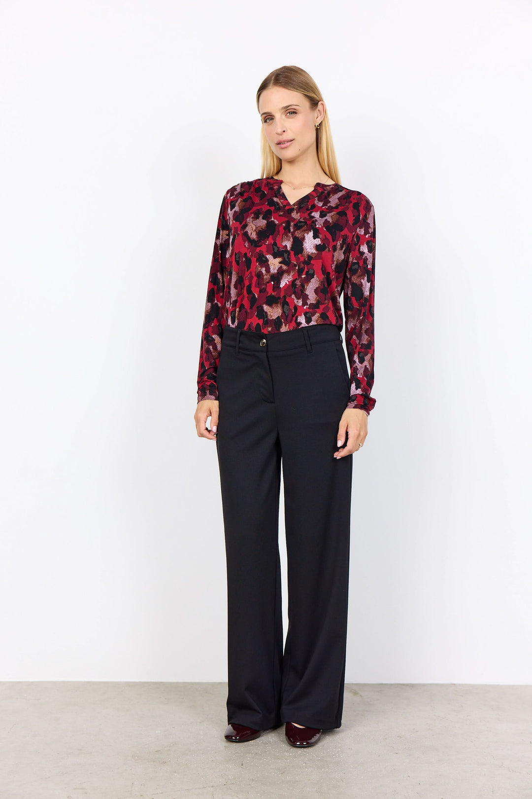 Femme portant une blouse imprimée abstraite avec encolure fendue et pantalon noir élégant.