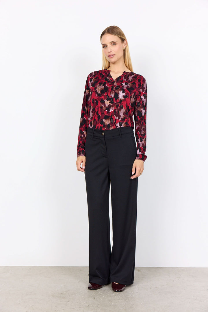 Femme portant une blouse imprimée abstraite avec encolure fendue et pantalon noir élégant.