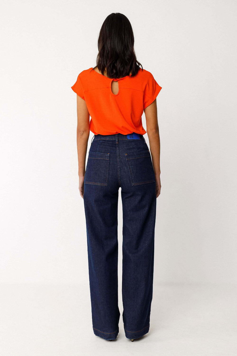Jeans Ainhize coupe large taille haute vue arrière, femme portant un haut orange, coupe fluide et poches arrière visibles.