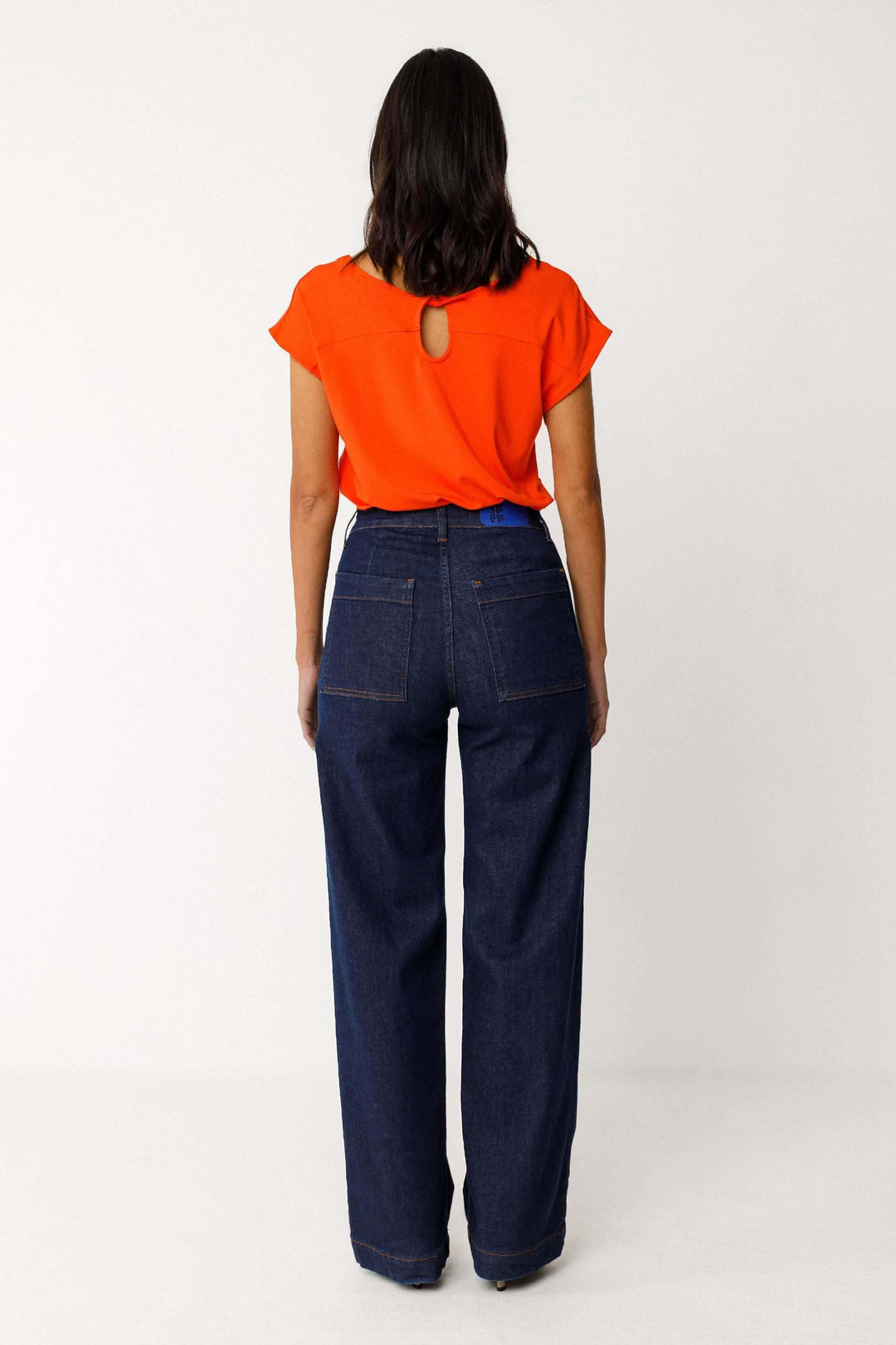 Jeans Ainhize coupe large taille haute vue arrière, femme portant un haut orange, coupe fluide et poches arrière visibles.