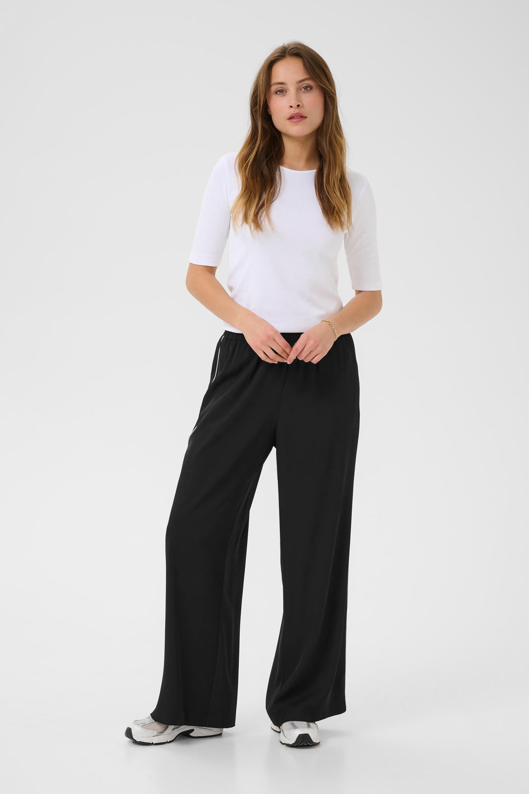 Femme portant le Pantalon Tessa fluide à jambe large, associé à un t-shirt blanc avec des baskets noires.