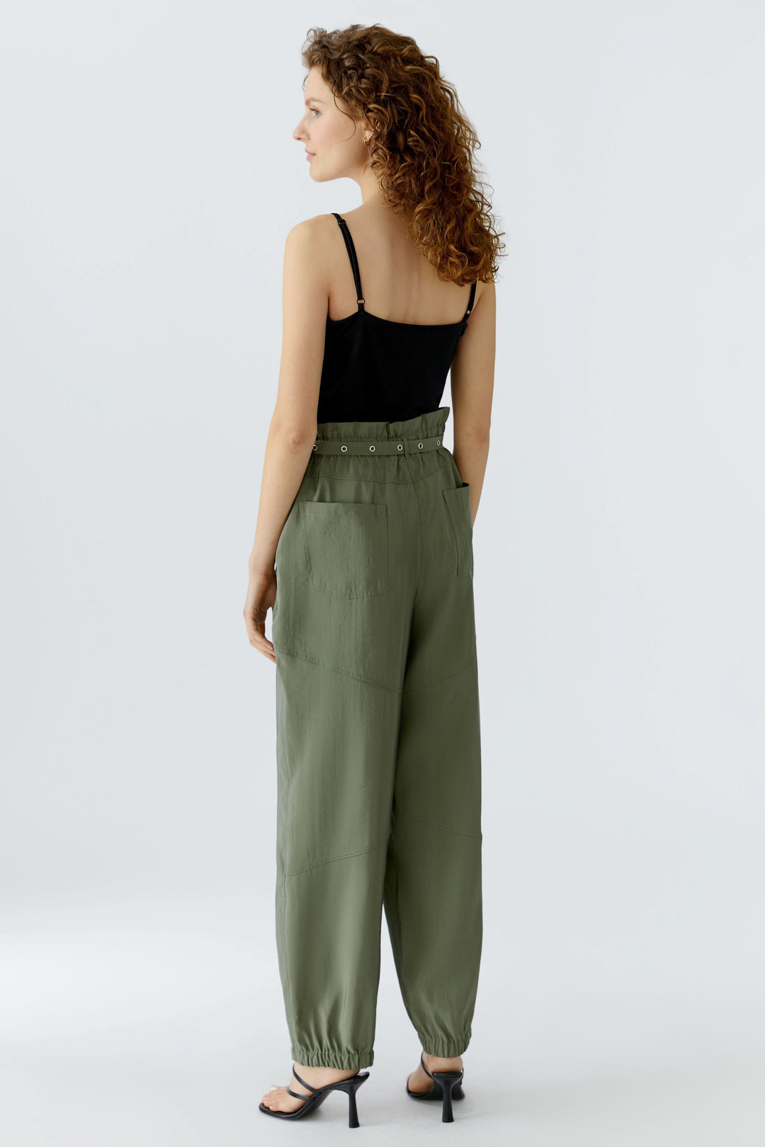 Femme portant un pantalon jogger ceinturé vert avec taille élastique et ceinture intégrée, vue de dos, sur fond blanc.