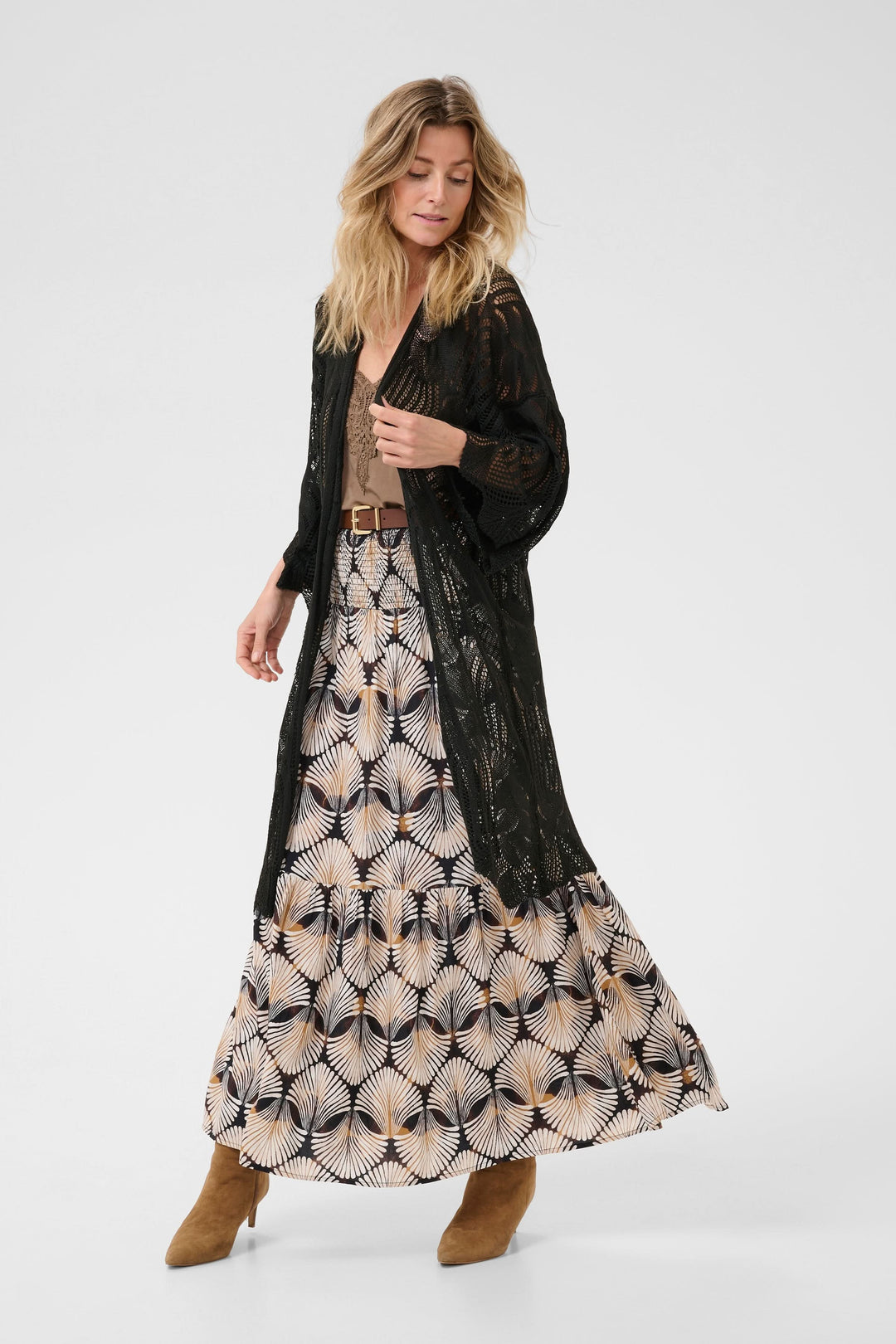Femme portant un cardigan long en tricot ajouré noir avec une jupe imprimée et des bottines en daim.