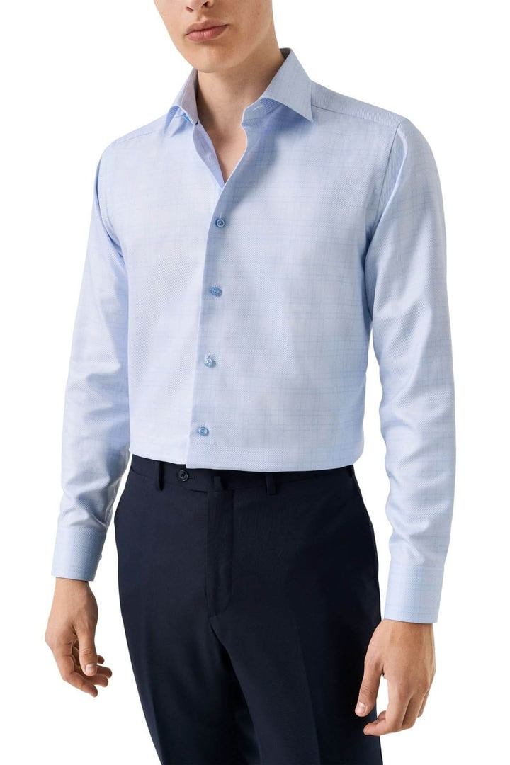 Chemise en coton bleu clair à carreaux fins portée par un modèle, avec un motif discret et une coupe sophistiquée, idéale pour le travail.