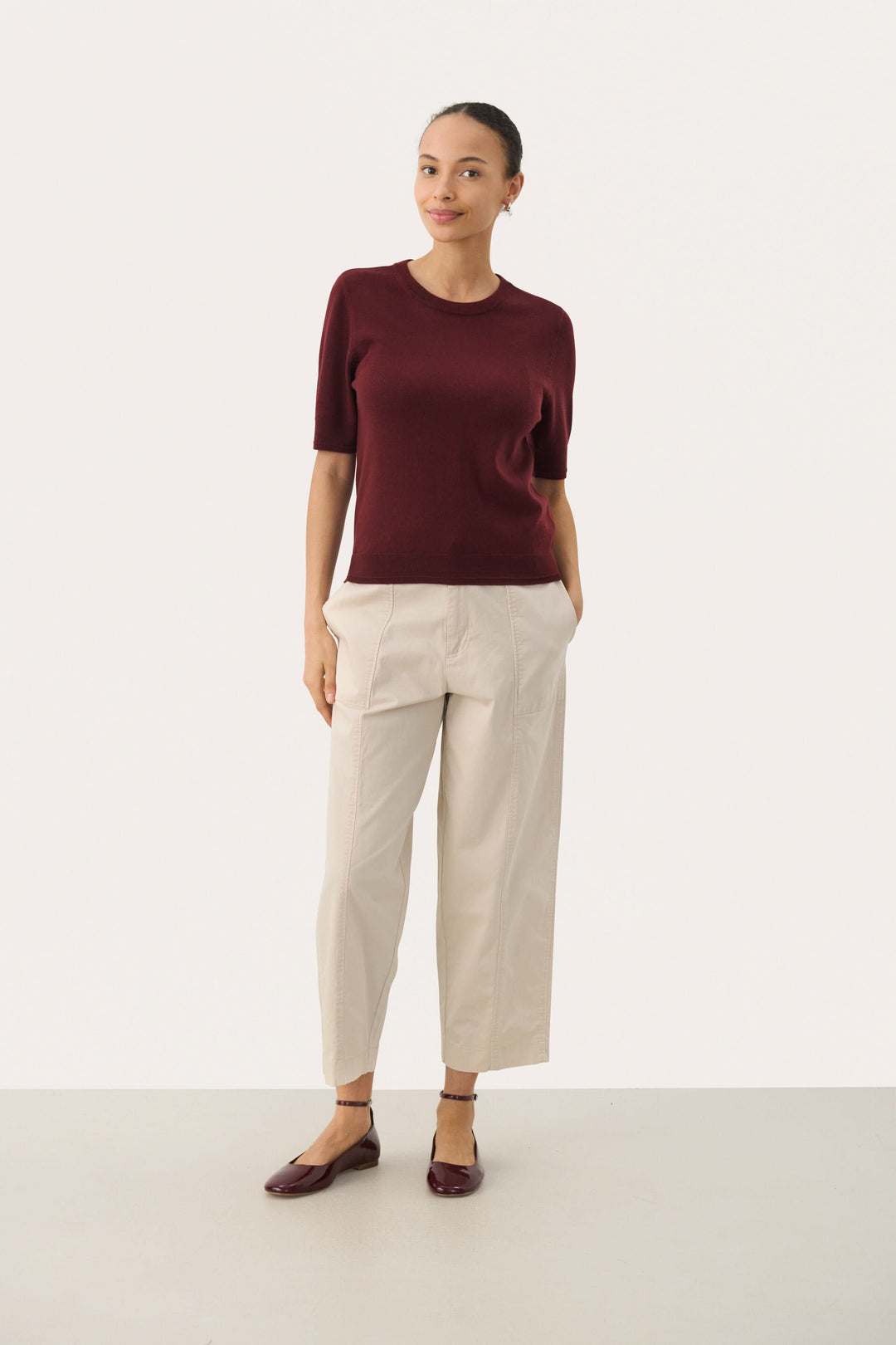 Chandail Natanya en tricot bordeaux à manches courtes, porté avec un pantalon clair pour un look élégant.