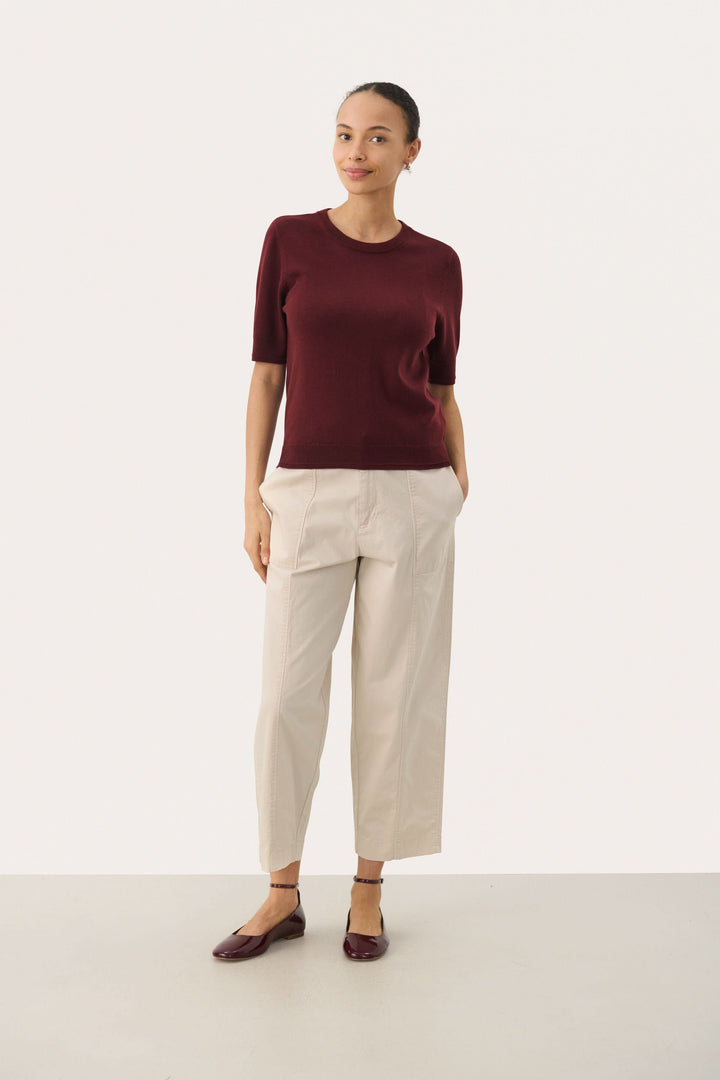 Chandail Natanya en tricot bordeaux à manches courtes, porté avec un pantalon clair pour un look élégant.
