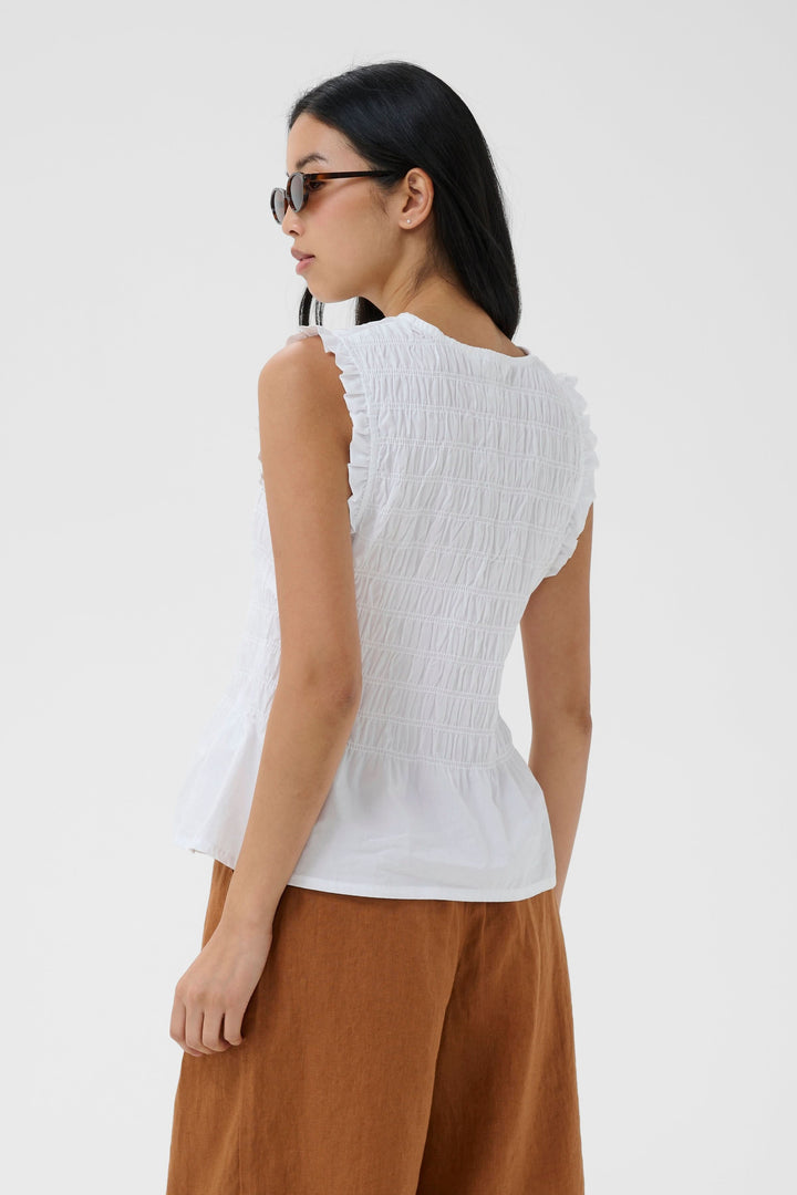Femme portant la Blouse Borgny smockée sans manches à encolure nouée, de dos, avec un effet smocké pour un style estival délicat.