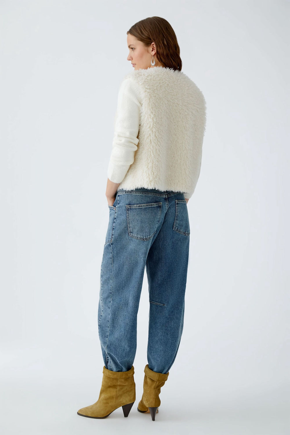 Femme vue de dos portant une veste sans manches en fausse fourrure avec un jean décontracté et des bottes à talons.