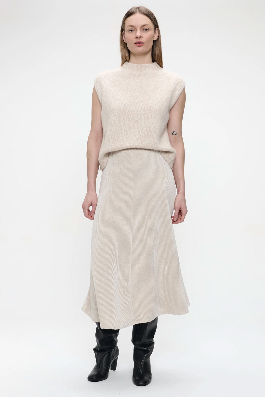 Femme portant une jupe midi en velours côtelé beige avec bottes hautes et un chandail léger, look élégant.