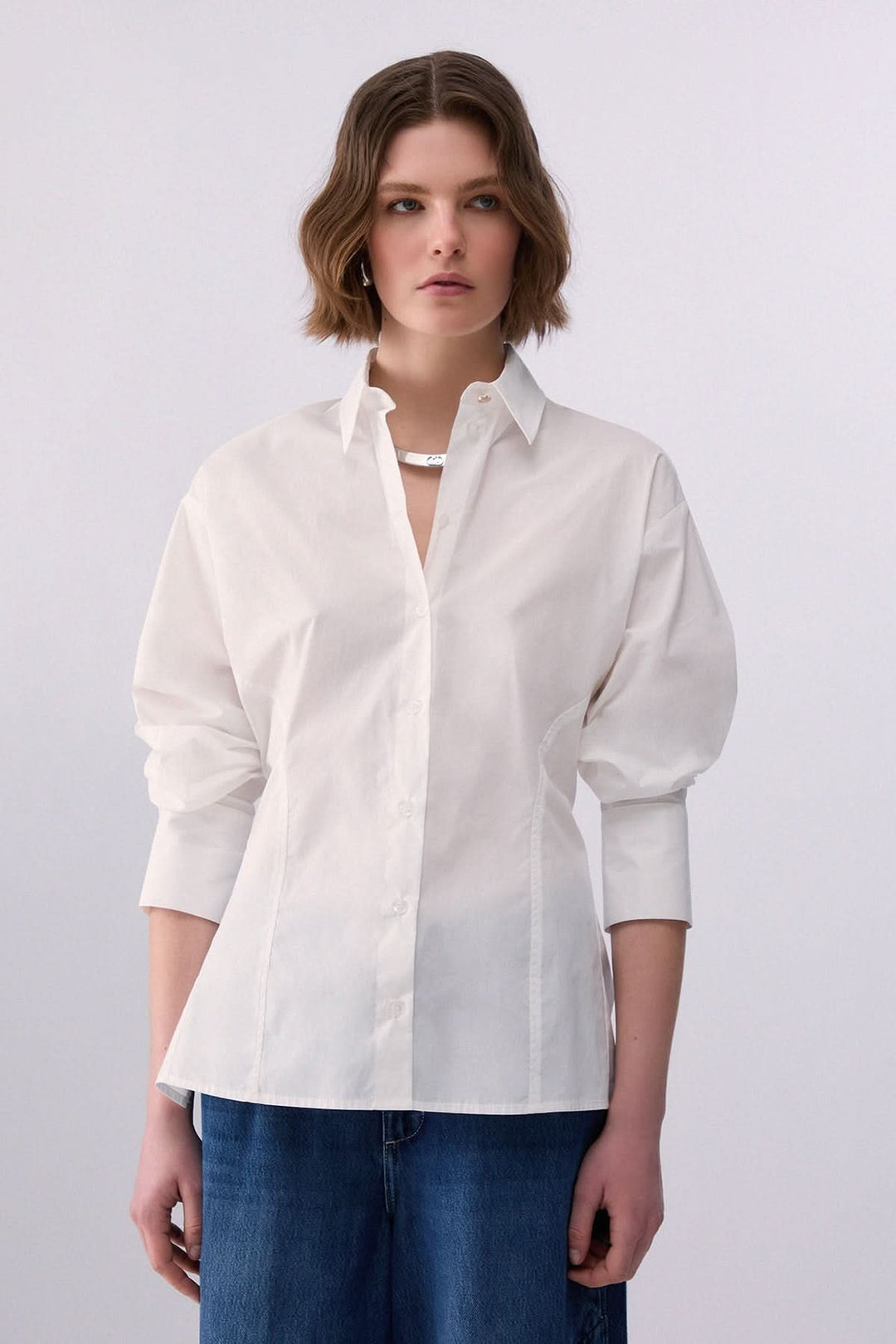 Femme portant une chemise à nouer au dos blanche avec manches longues et col classique, idéal pour un style structuré et moderne.