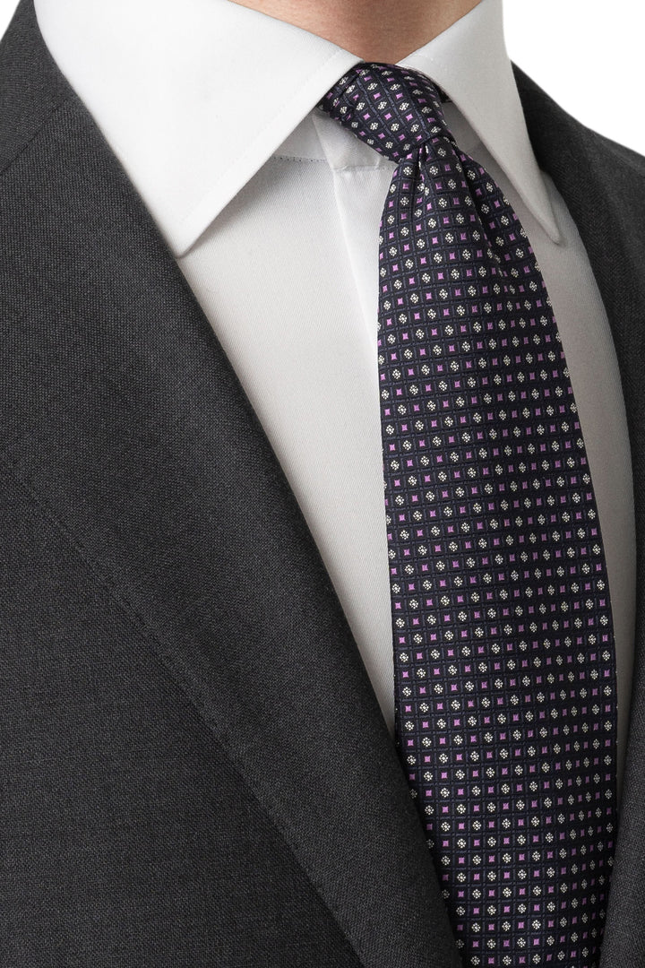 Cravate géométrique en satin aux teintes violet et blanc, portée avec une chemise blanche et un costume sombre.