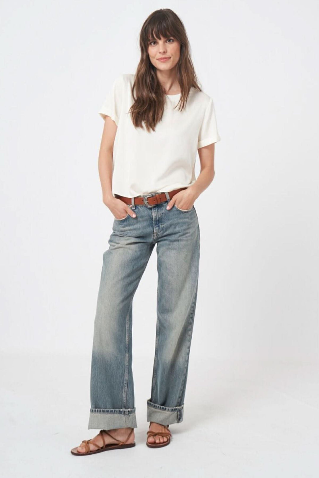 Femme portant un jean ample et une blouse en soie blanche, tenue décontractée et chic, manches courtes, sandales marron.
