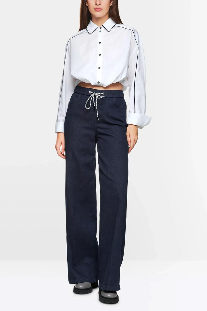 Femme portant un haut blanc à boutons et un jean évasé bleu marine avec ceinture élastique, style moderne.