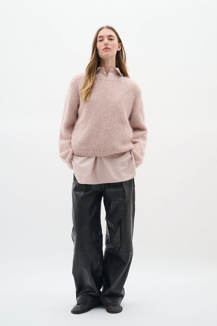 Chandail Jetra en maille duveteuse rose, porté avec une chemise beige et un pantalon noir, pour un look cosy et élégant.