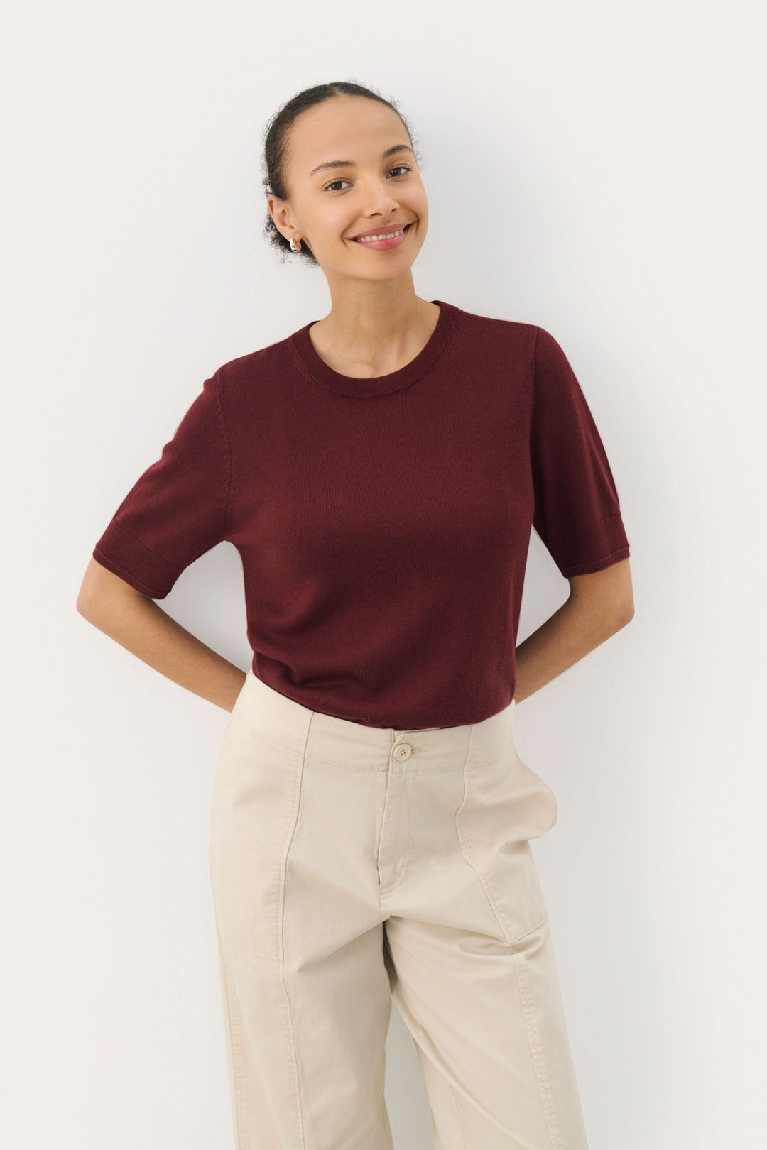Chandail Natanya en laine bordeaux à manches courtes et encolure ronde, porté avec un pantalon clair.