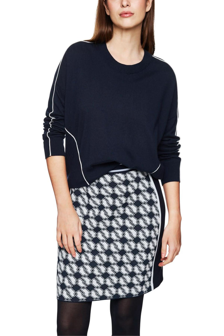 Pull en laine et cachemire avec passepoils contrastés, porté avec une jupe à motifs, créant un look moderne.