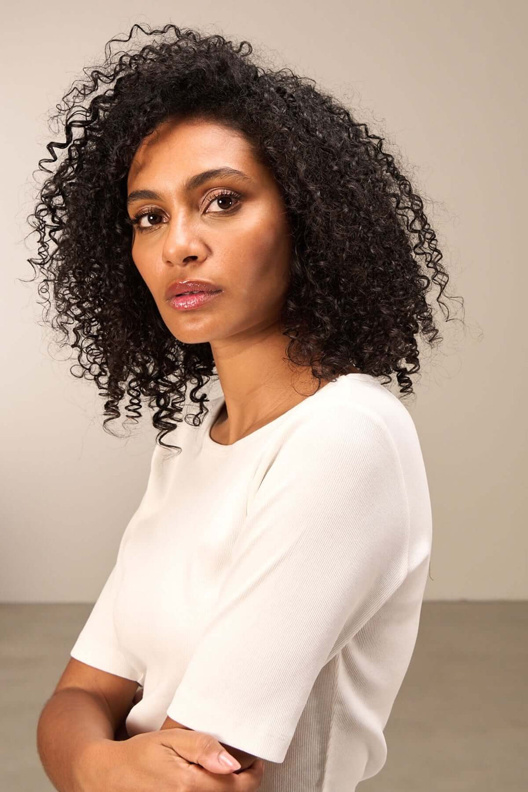 Femme avec cheveux bouclés portant un chandail à manches courtes, regardant la caméra avec élégance.