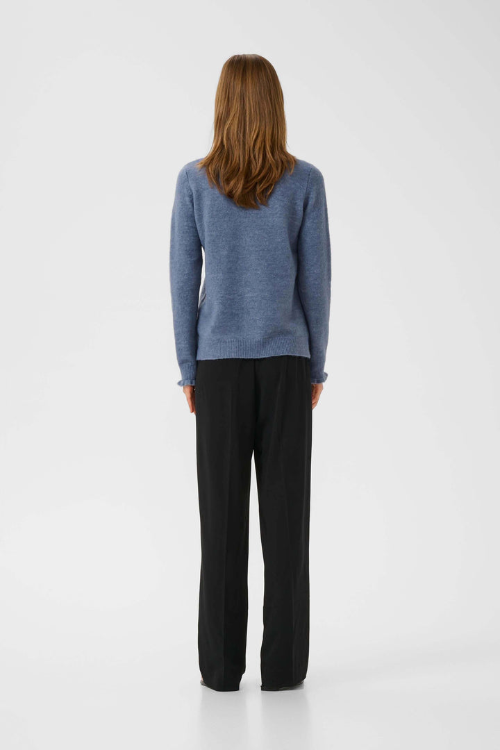 Femme de dos portant un tricot Guni à col montant froncé et un pantalon fluide, style chic décontracté.