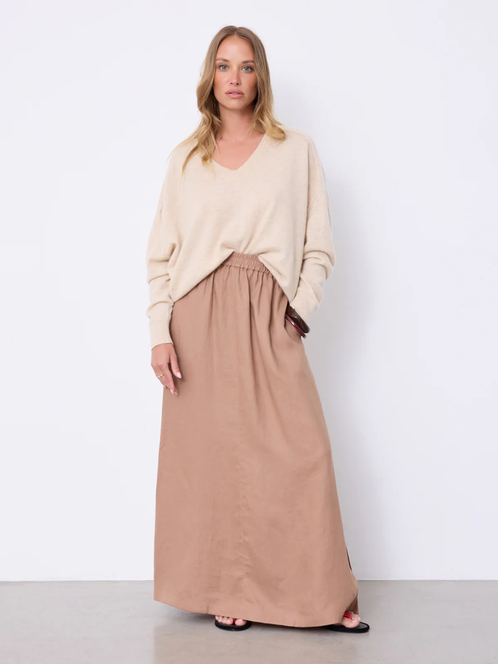Femme portant Jupe Vivienne longue fluide taille élastique avec haut beige, tenue élégante et estivale, détails fente et poches visibles.