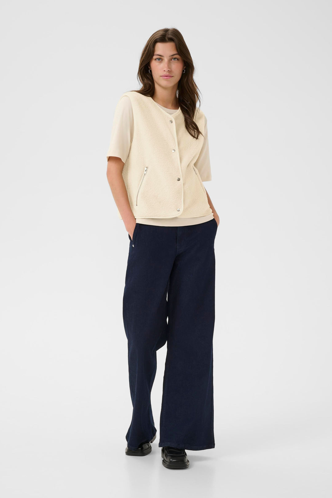 Femme portant une veste sans manches beige et un pantalon large bleu marine, style décontracté et moderne.