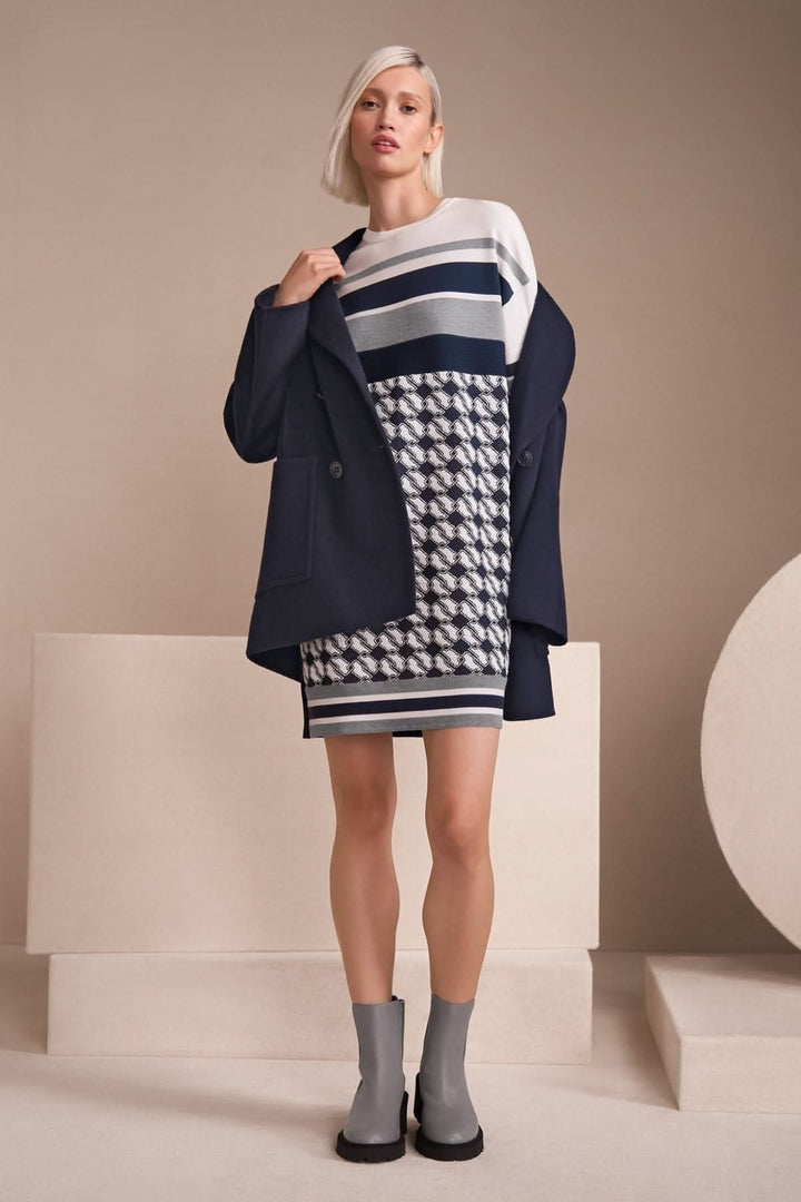 Femme portant une robe imprimée à motif géométrique, associée à un blazer, sur fond neutre.