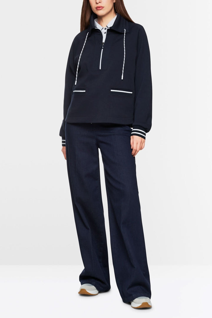 Sweat-shirt zippé ample en coton avec col à cordon, poches et bordures rayées, portés avec un pantalon décontracté.