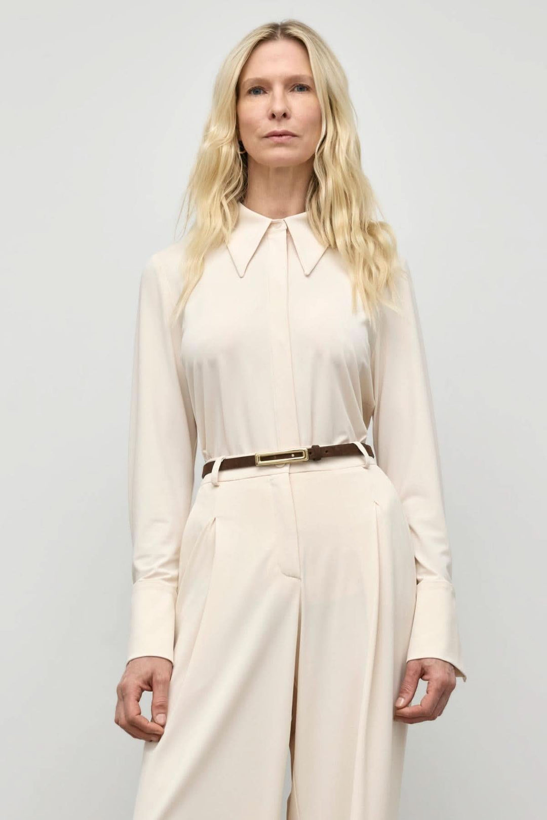 Chemisier en jersey mat avec col prononcé porté par modèle en pantalon taille haute, look moderne et élégant.