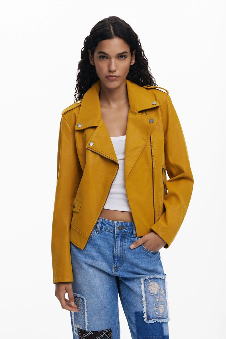 Veste en cuir jaune à col biker, portée avec un top blanc et un jean décontracté, style moderne et audacieux.