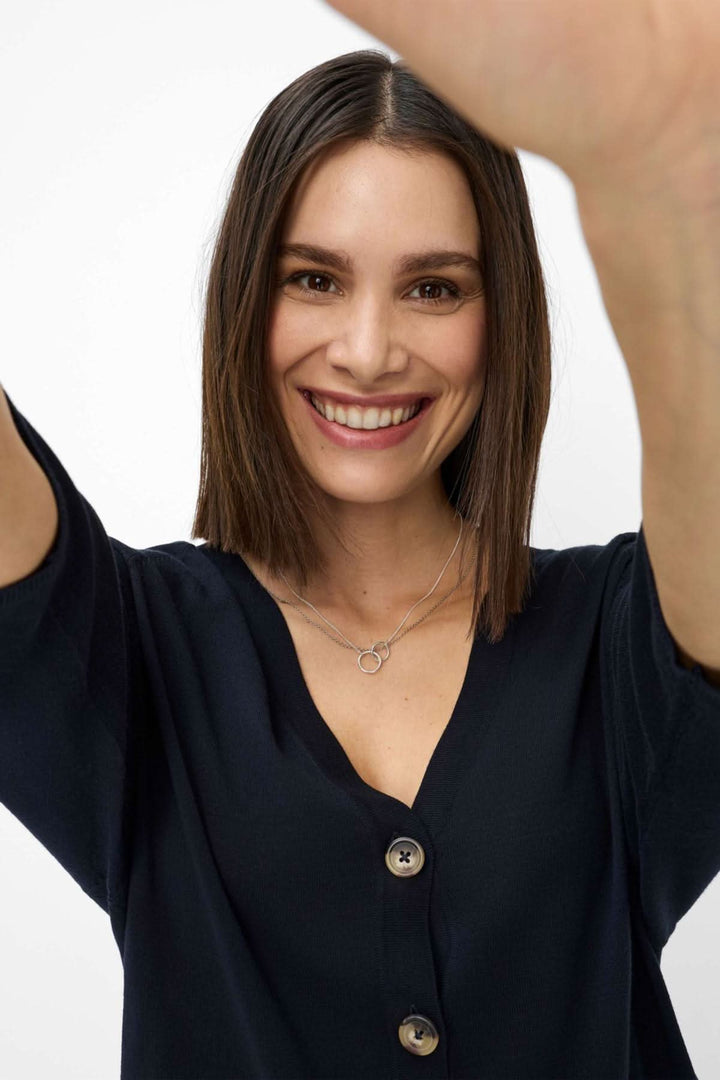 Femme souriante posant en cardigan Anique avec une encolure V, mettant en valeur un look élégant et décontracté.