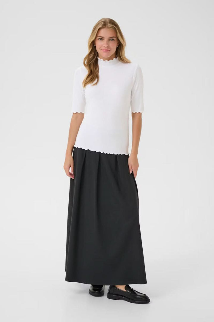 Femme portant un T-shirt Ribba blanc à col montant festonné, maille côtelée, manches mi-longues, avec jupe longue noire et mocassins.