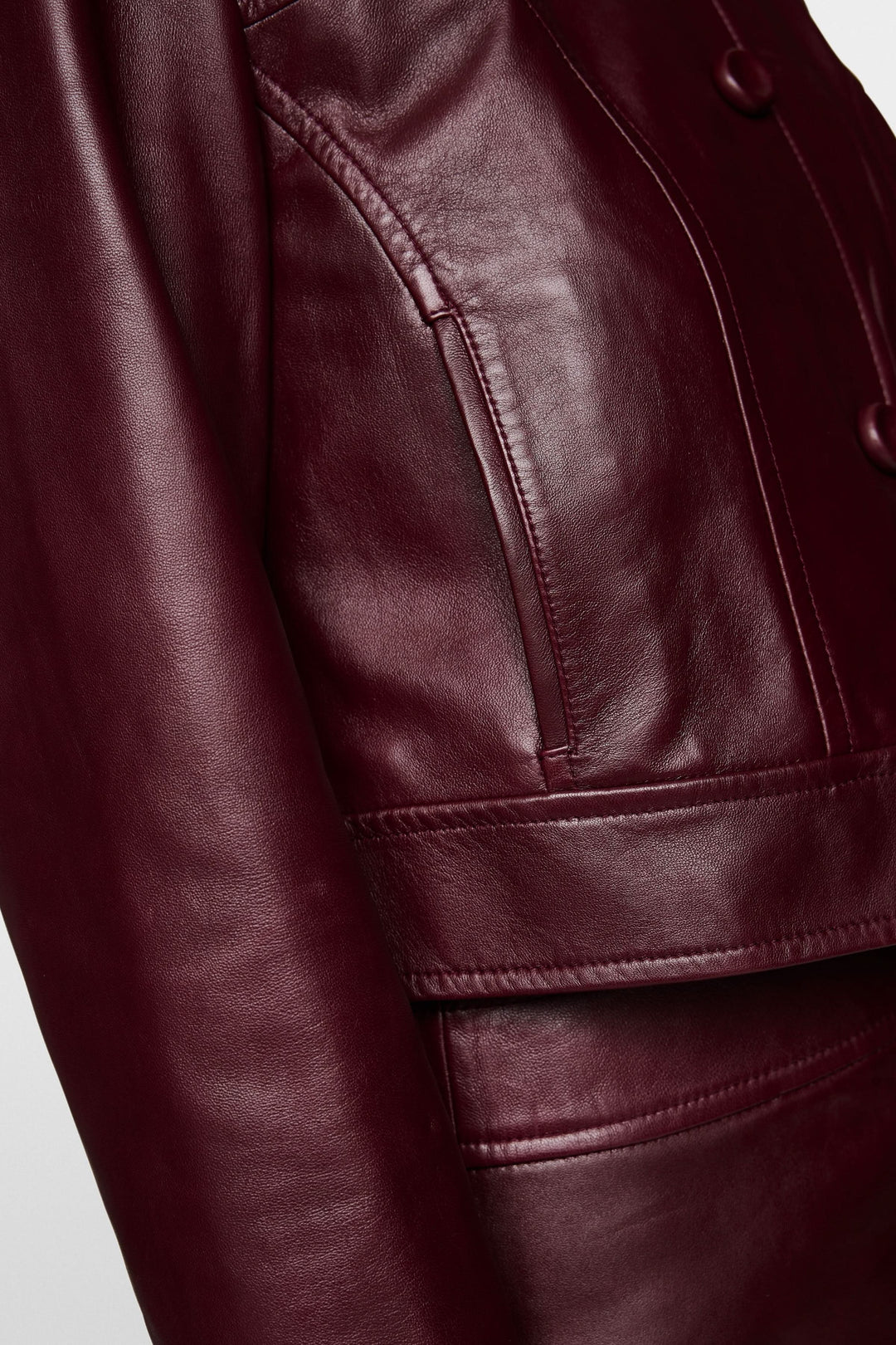 Détail d'une veste en cuir bordeaux avec fermeture à boutons et poches pratiques.