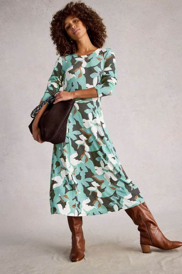 Robe Madeline à col rond et manches longues en jersey, imprimé graphique, coupe évasée, portée avec bottes et sac à main.