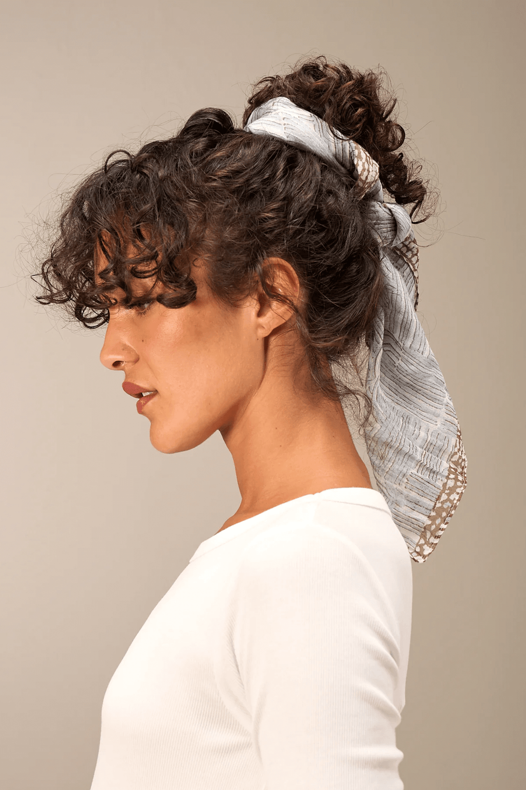 Foulard imprimé léger et texturé, porté en accessoire cheveux, rehausse un look moderne et raffiné.