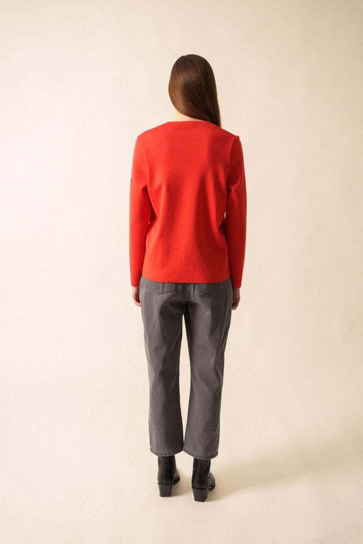 Femme vue de dos portant un gilet en laine rouge et un pantalon gris, dans un style élégant et décontracté.