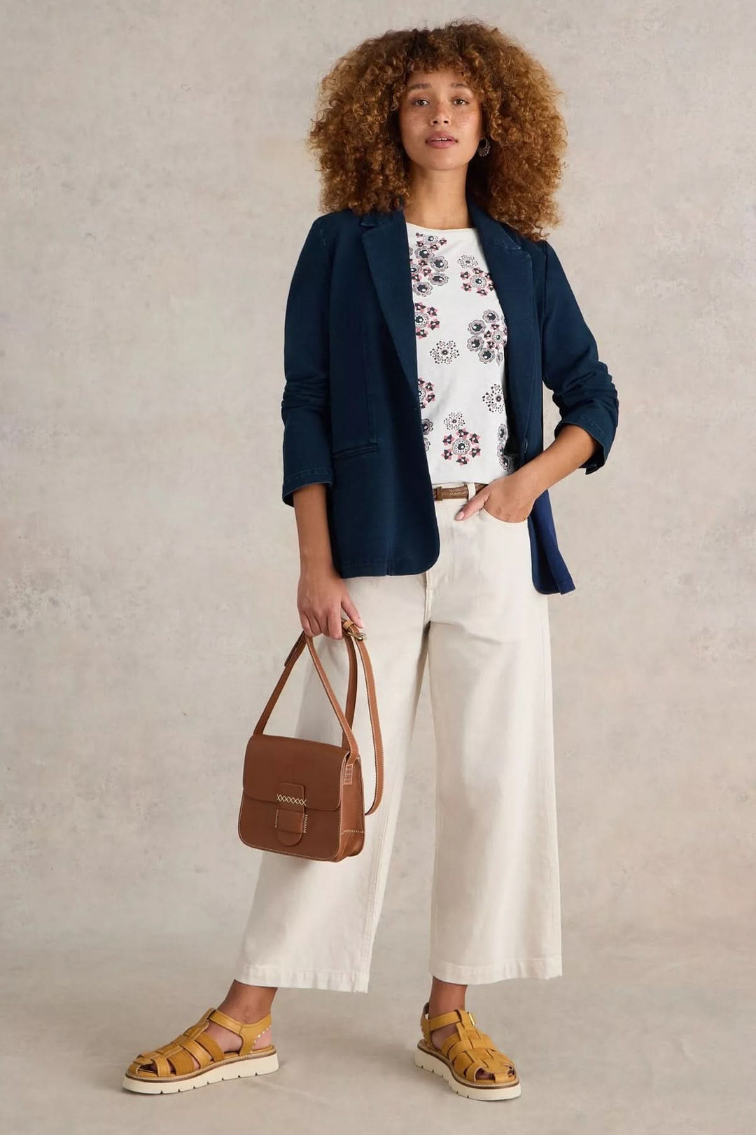 Femme stylée en veston décontracté bleu, t-shirt imprimé, pantalon clair et sac caramel.