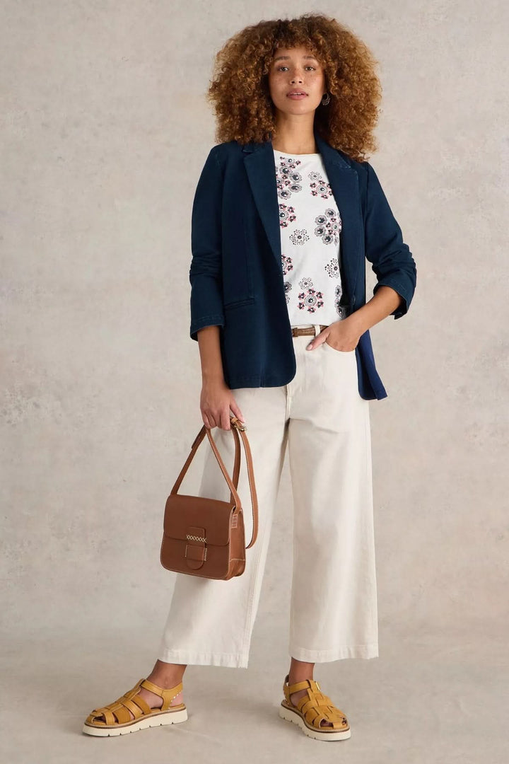 Femme stylée en veston décontracté bleu, t-shirt imprimé, pantalon clair et sac caramel.