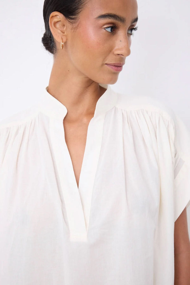 Femme portant une Robe Fani courte fluide col ouvert avec col en V et manches courtes, élégance minimaliste, vue de face.