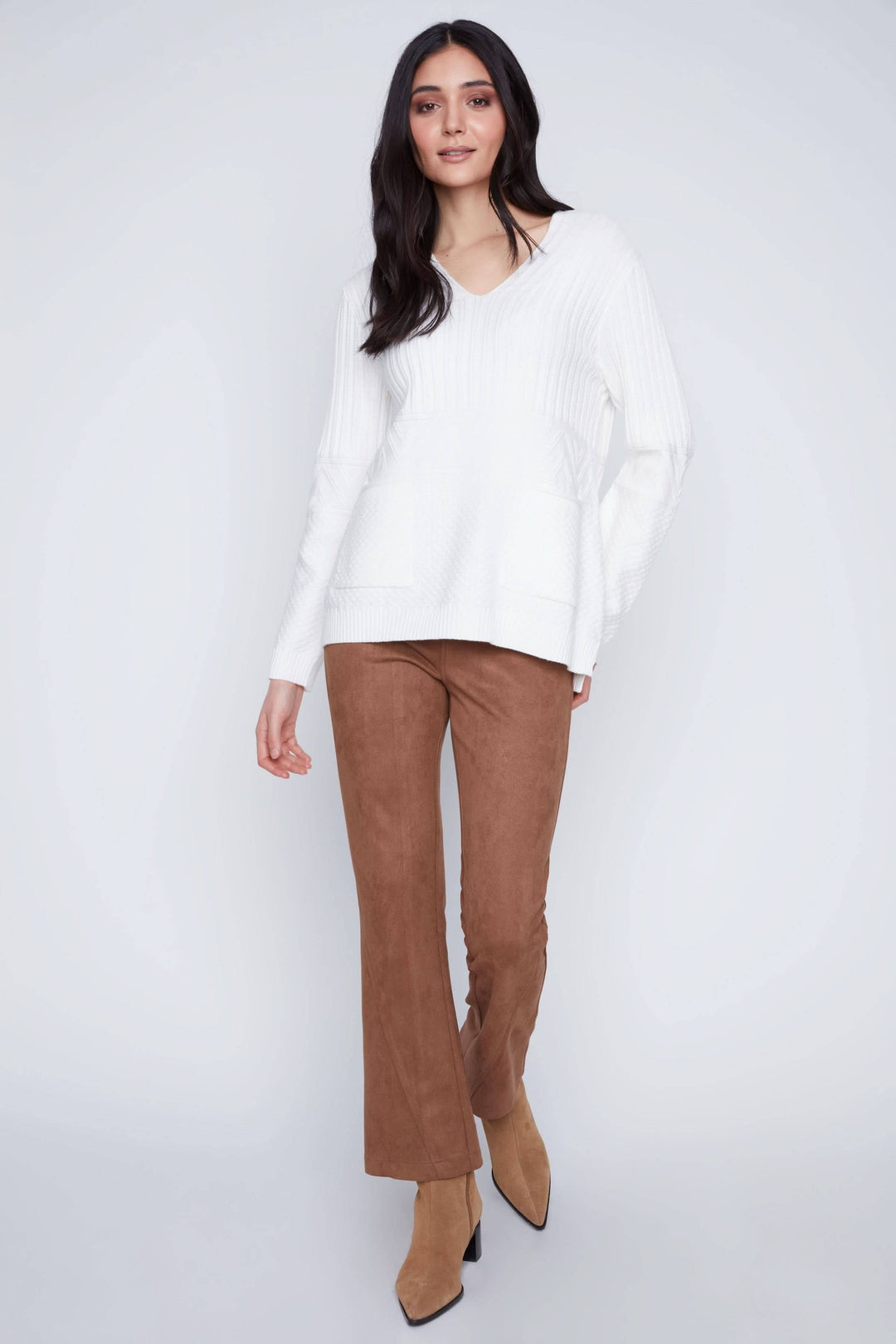 Femme portant une tunique en tricot blanche avec encolure en V et pantalon marron, style décontracté et élégant.