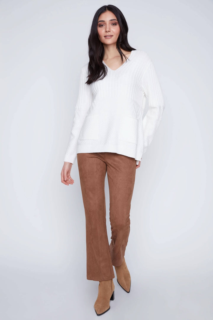 Femme portant une tunique en tricot blanche avec encolure en V et pantalon marron, style décontracté et élégant.