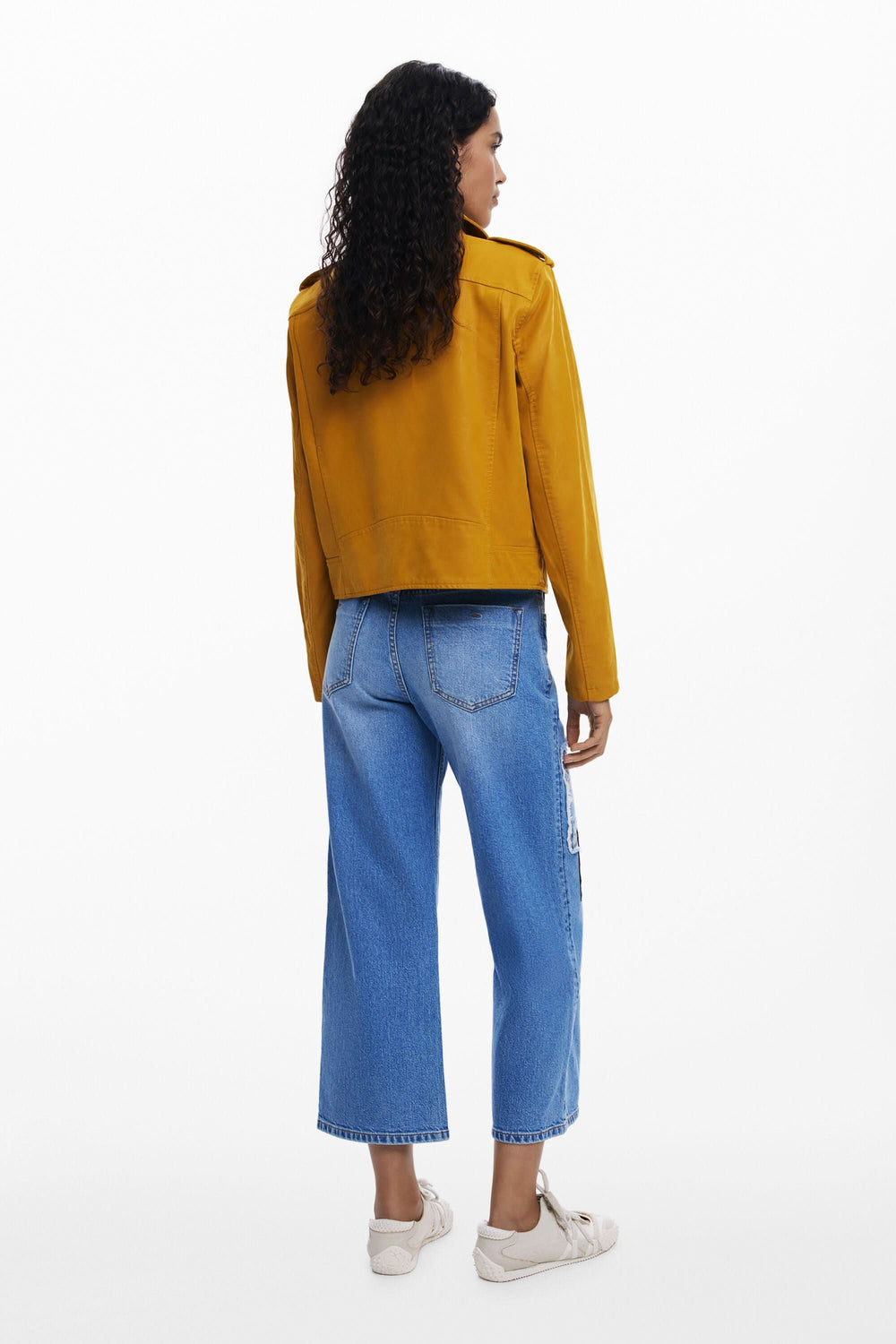 Femme vue de dos portant une veste jaune avec un jean à broderies, mode créative et moderne.