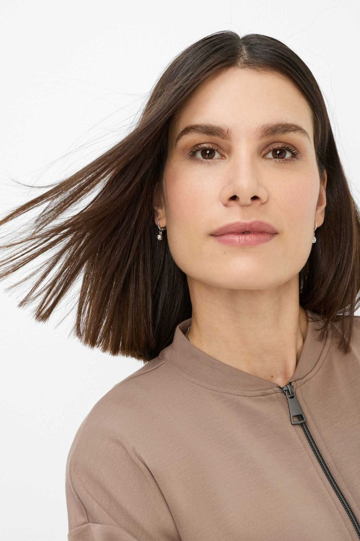 Portrait d'une femme portant une veste beige, cheveux longs flottants, affichant une allure moderne et naturelle.