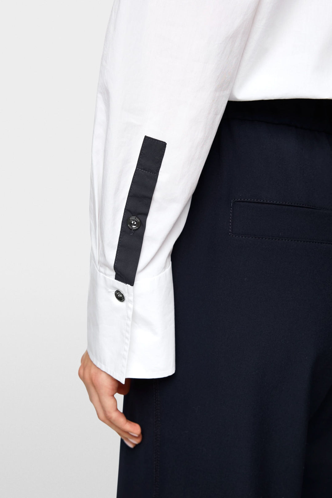 Détail de la manche d'une chemise blanche avec boutons contrastants sur un pantalon noir.